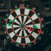 Close-up of a dartboard with red and green darts hitting various spots, indoors setting.
